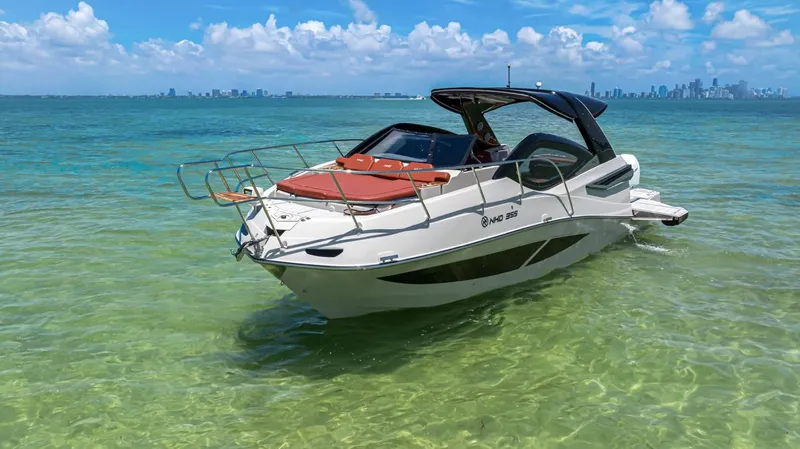  Yacht Photos Pics 2024 NHD 355 Open Deck boat on clear turquoise water, city skyline in background.