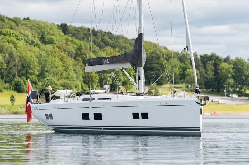  Yacht Photos Pics 2019 Hanse 548 yacht sailing on calm waters near a lush, green shoreline.
