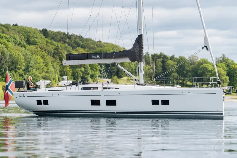  Yacht Photos Pics 2019 Hanse 548 yacht sailing on calm waters with lush green forest backdrop.