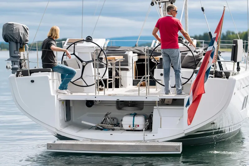  Yacht Photos Pics 2019 Hanse 548 yacht with two people steering, featuring a flag and open storage compartment.