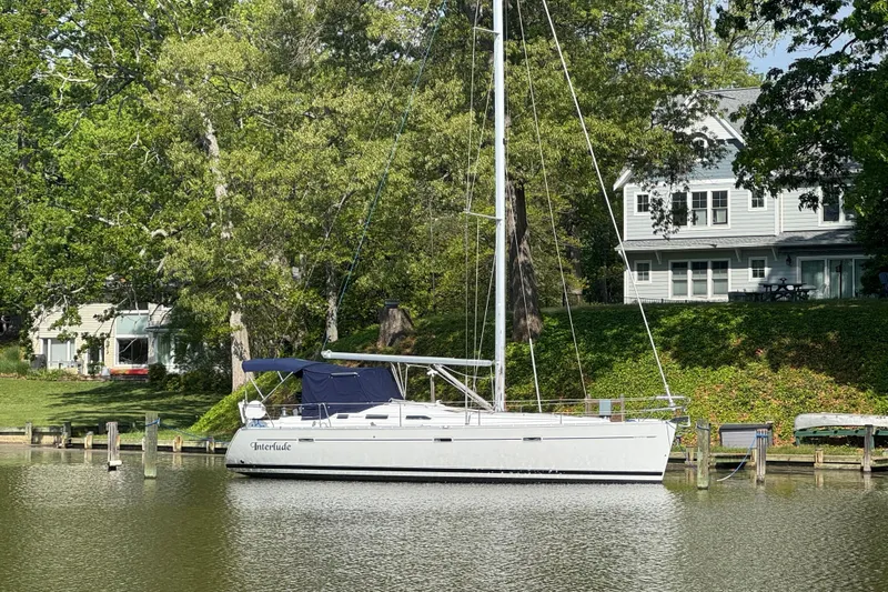 Interlude Yacht Photos Pics Beneteau Oceanis 393 sailboat docked by a lakeside house, surrounded by lush greenery.
