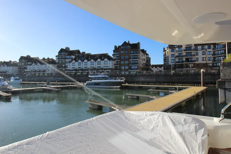  Yacht Photos Pics Modern marina with 2024 Prestige 520 yacht, surrounded by waterfront buildings under clear blue sky.