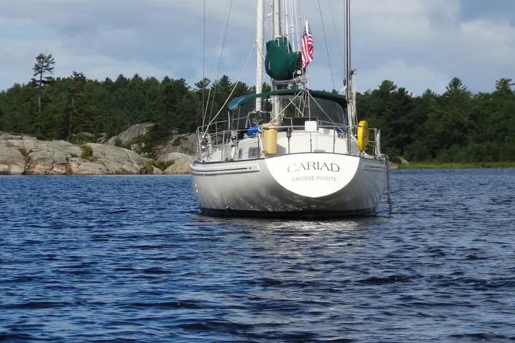 Sailboat "Cariad" on water, Rival 41C model, 1978, with forested shoreline background.