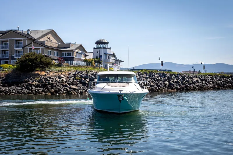 Noor Yacht Photos Pics 2023 Tiara Yachts C44 Coupe cruising near coastal buildings and rocky shoreline.