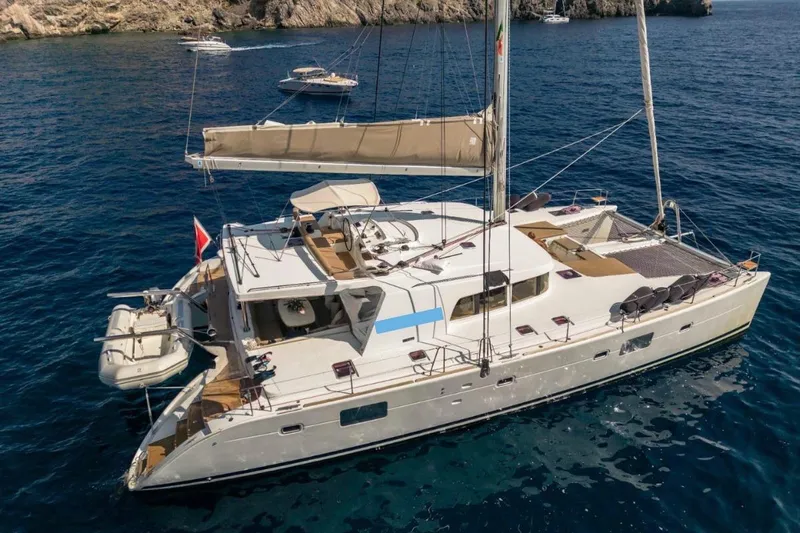  Yacht Photos Pics 2011 Lagoon 500 catamaran sailing on clear blue waters near rocky coastline.