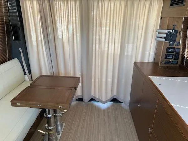 This Could Be Yours Yacht Photos Pics Interior of 2023 Bavaria R40 Coupe with wooden table, white seating, and curtains.