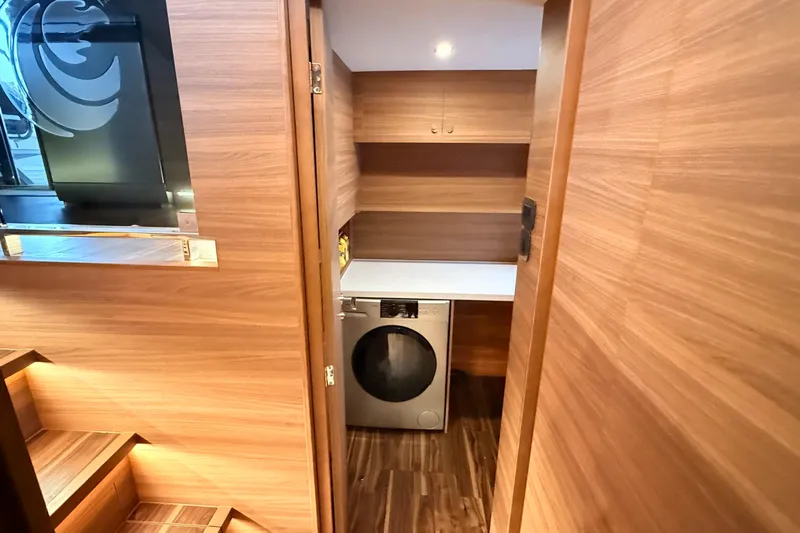  Yacht Photos Pics Laundry area inside 2025 Aquila 50 Yacht, featuring modern wood paneling and a washing machine.