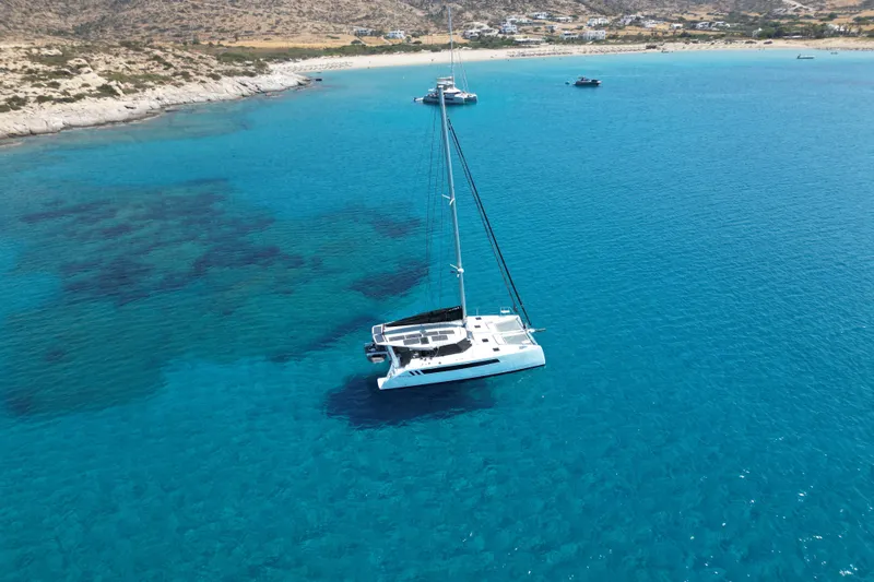 Ruby Rose 2 Yacht Photos Pics 2023 Seawind 1370 catamaran sailing in clear blue waters near rocky coastline.