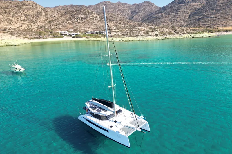 Ruby Rose 2 Yacht Photos Pics 2023 Seawind 1370 catamaran sailing in clear turquoise waters near rocky coastline.
