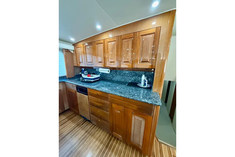 Kickback Yacht Photos Pics Luxurious kitchen interior of 2004 Viking 65 Convertible yacht with wooden cabinets and granite countertops.