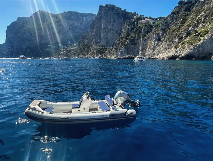 Lady Amanda Yacht Photos Pics Inflatable boat on blue water near rocky cliffs, sunny day.