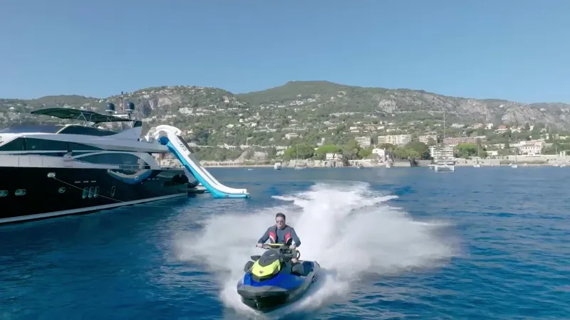 Lady Amanda Yacht Photos Pics Man on jet ski near 2006 Couach 2800 yacht with slide, scenic coastal backdrop.