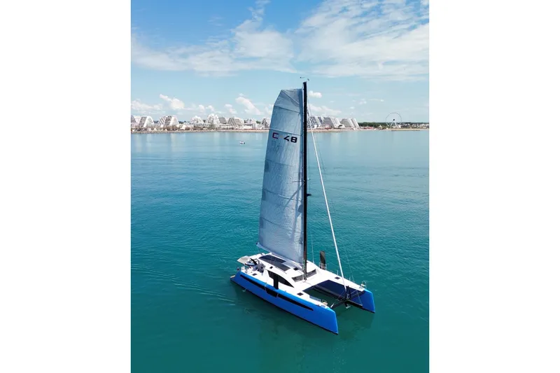 Aurora Yacht Photos Pics 2025 C-Catamarans 48 sailing on calm blue waters near a coastal cityscape.