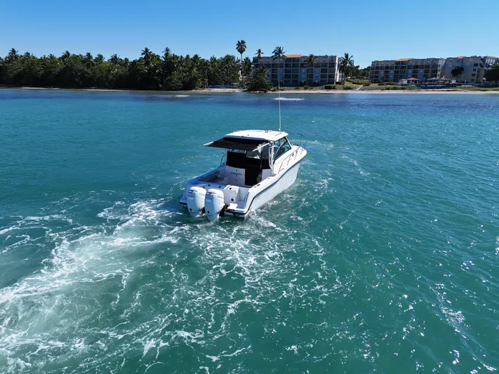  Yacht Photos Pics 2015 Boston Whaler 315 Conquest cruising on clear blue water near a tropical shoreline.