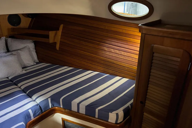 Pirouette Yacht Photos Pics Cozy cabin interior of 2003 Hinckley 36 Picnic Boat EP with striped bedding and wooden paneling.