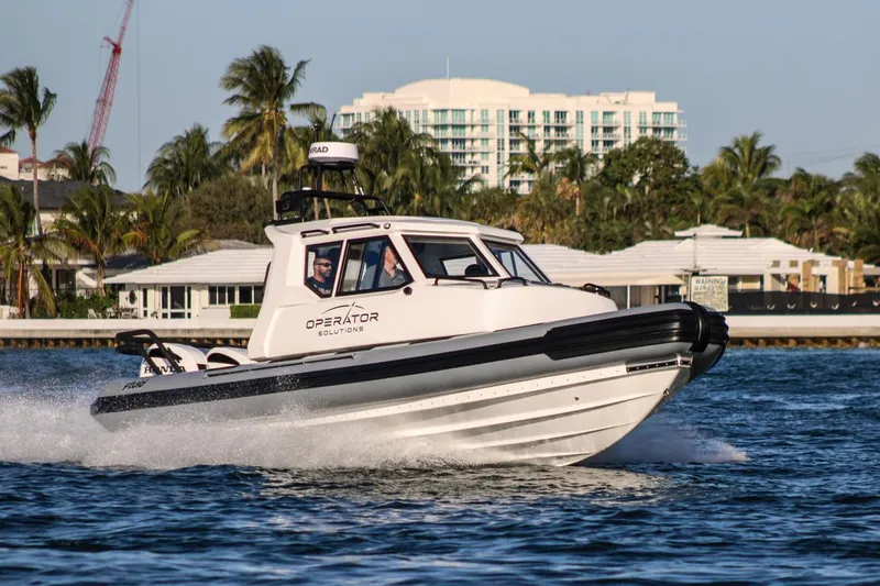 Operator 01 Yacht Photos Pics 2022 Fluid Watercraft Patrol 880 Cabin boat cruising on water near palm trees and buildings.