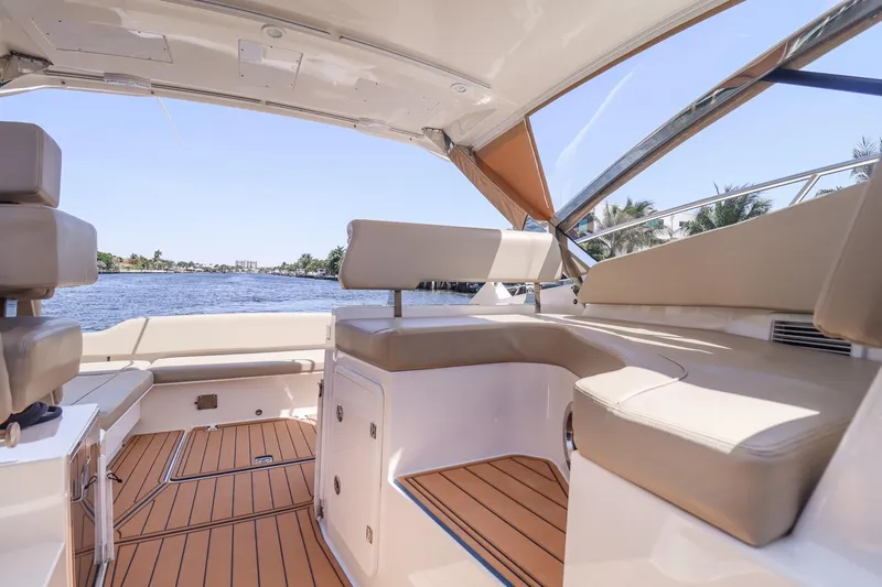 Ocean's Grace Yacht Photos Pics 2016 Pursuit SC 365i boat interior with beige seating and wooden flooring, overlooking a serene water view.