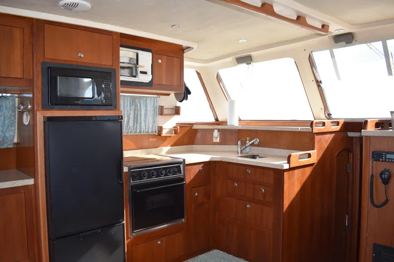  Yacht Photos Pics 2001 Mainship 390 yacht kitchen with wood cabinetry, microwave, fridge, stove, and sink.