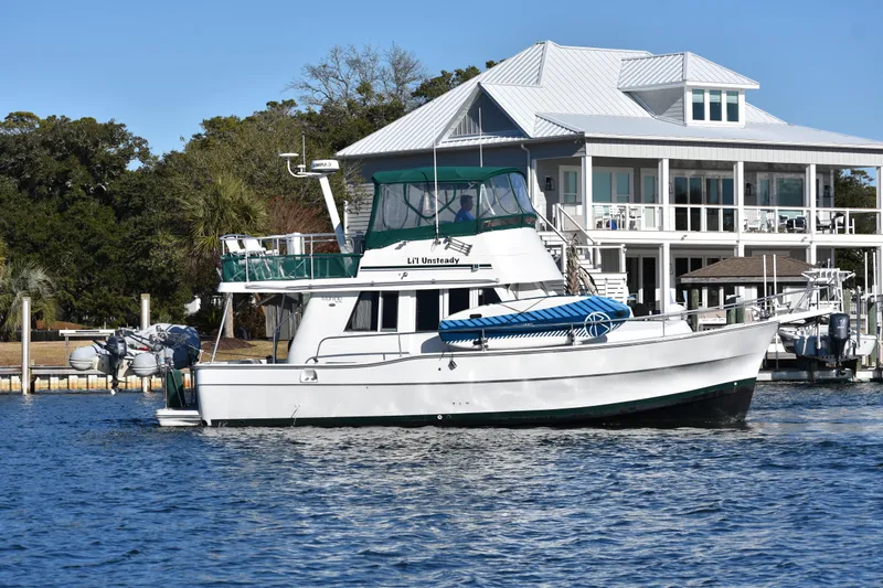  Yacht Photos Pics 2001 Mainship 390 yacht docked near a waterfront house, with clear blue skies.