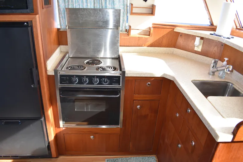  Yacht Photos Pics 2001 Mainship 390 yacht kitchen with stove, sink, and wooden cabinetry.