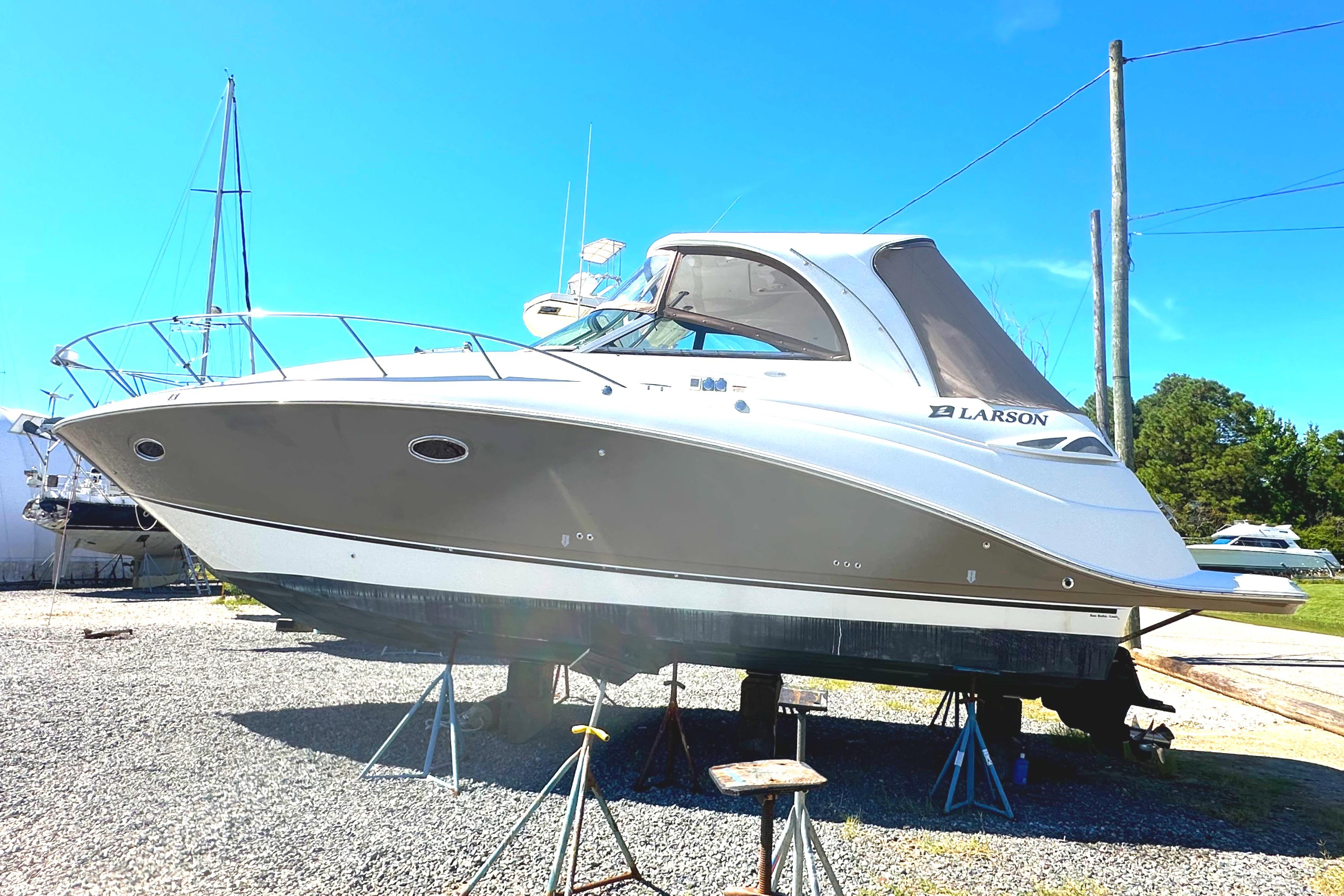 2006 Larson Cabrio 350 boat on stands, displayed outdoors under clear blue sky.