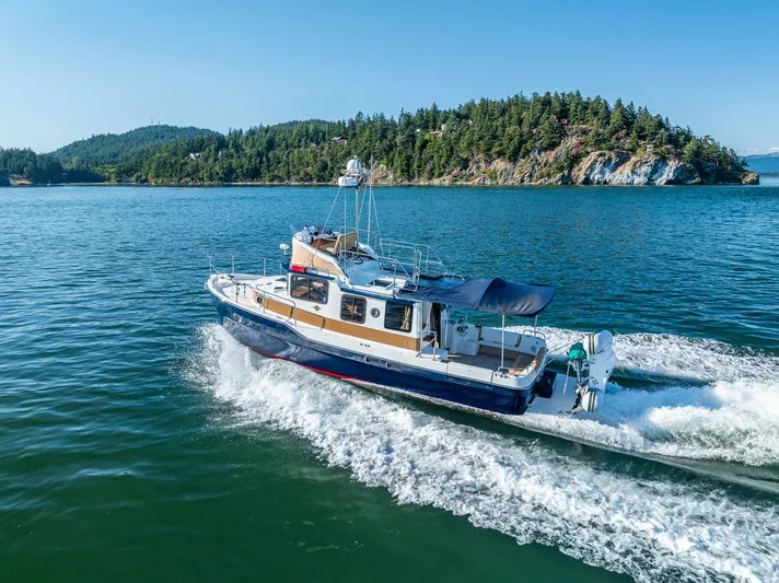 The Western Yacht Photos Pics 2014 Ranger Tugs R-31CB cruising on scenic blue waters near forested island.