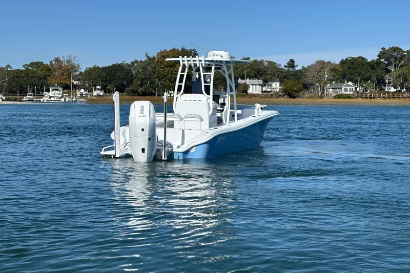  Yacht Photos Pics 2026 Yellowfin 26 Hybrid boat on calm water, surrounded by trees and houses.
