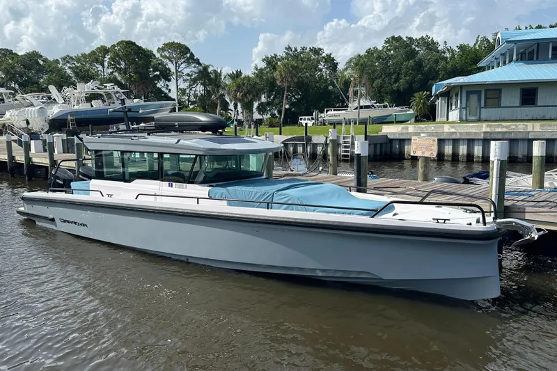  Yacht Photos Pics 2024 Axopar 37XC boat docked at marina, surrounded by trees and buildings.