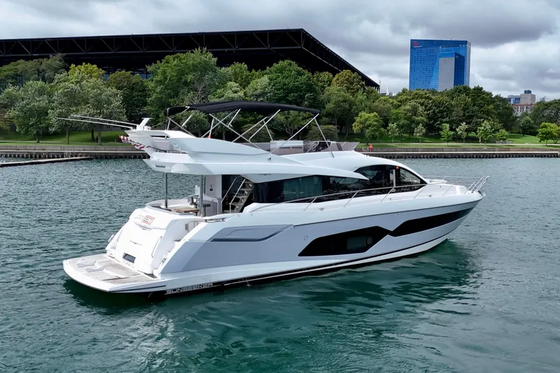  Yacht Photos Pics 2019 Sunseeker Manhattan 66 yacht on water, with lush greenery and cityscape background.