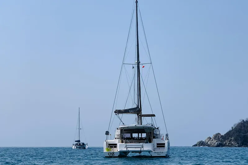 Oz Yacht Photos Pics Catamaran Bali 4.1 sailing on calm sea, 2019 model, with distant boat and rocky shoreline.