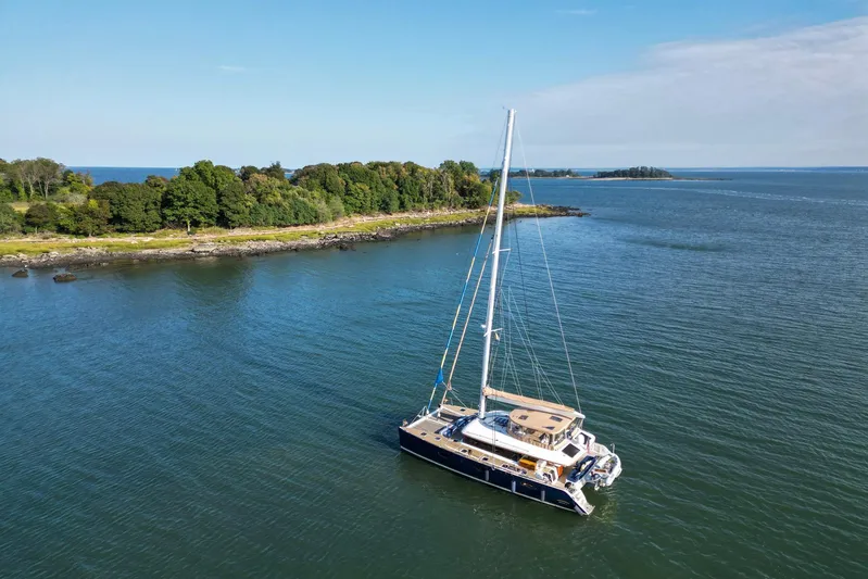 Andromeda Yacht Photos Pics 2016 Lagoon 620 catamaran sailing near a lush, green island under a clear blue sky.