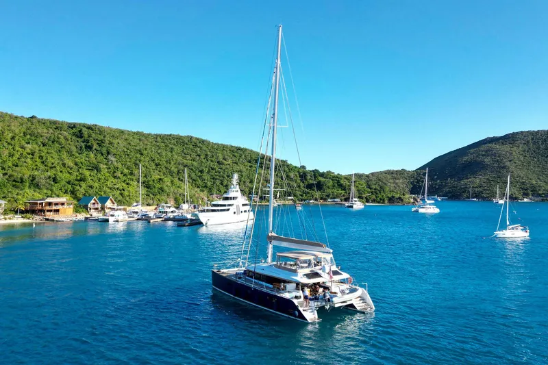 Andromeda Yacht Photos Pics Sailing catamaran Lagoon 620, 2016 model, anchored in a scenic bay with lush hills.