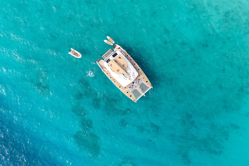 Andromeda Yacht Photos Pics Aerial view of 2016 Lagoon 620 yacht on turquoise water with small boat nearby.