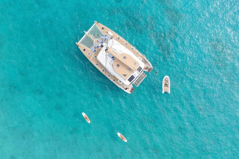 Andromeda Yacht Photos Pics Aerial view of 2016 Lagoon 620 catamaran on turquoise water with small boats nearby.