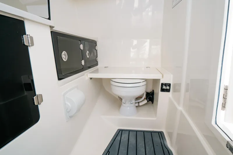 + Sea Keeper 2 Yacht Photos Pics 2024 Cobia 330 Dual Console boat interior with compact marine toilet and storage cabinets.