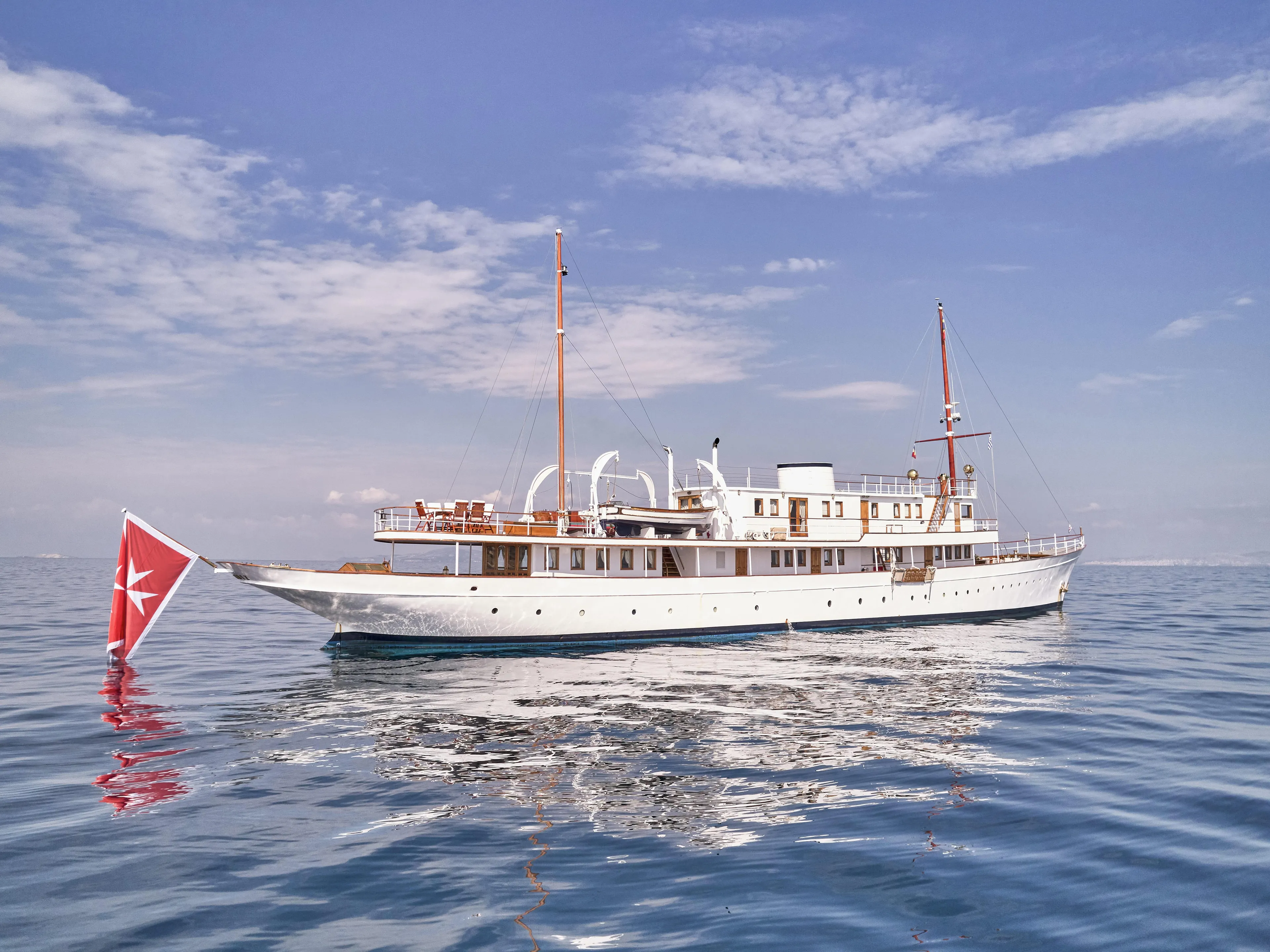 Vintage 1902 Ailsa Shipbuilding yacht on calm sea under clear sky.