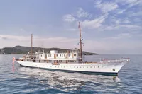 Historic 1902 Ailsa Shipbuilding yacht on calm sea with scenic background.