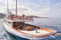 Vintage 1902 Ailsa Shipbuilding yacht with wooden deck, sailing on calm sea under a partly cloudy sky.