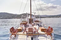 Historic 1902 Ailsa Shipbuilding yacht with elegant deck chairs, scenic coastal backdrop.