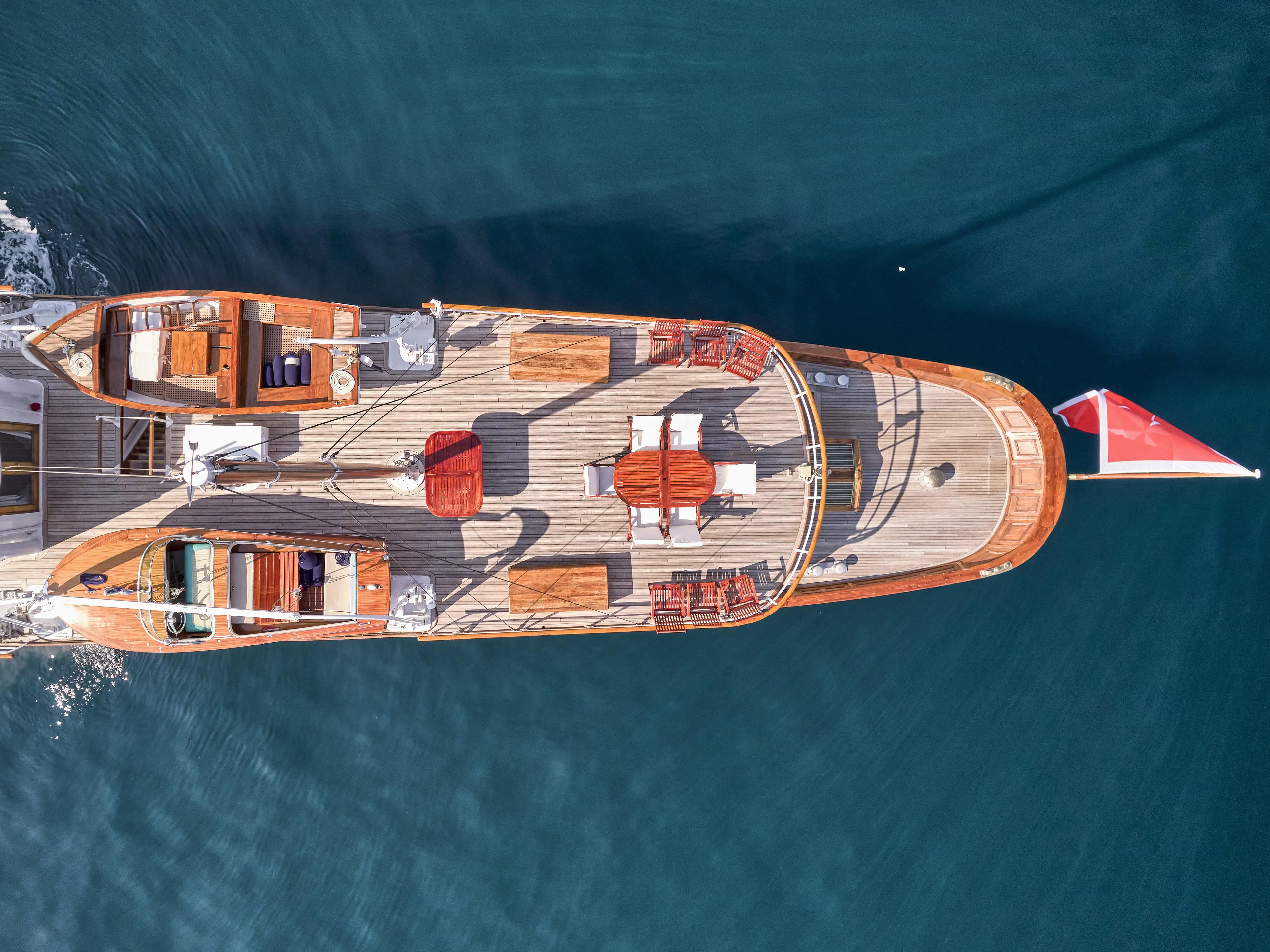 Aerial view of a 1902 Custom Ailsa Shipbuilding yacht with wooden deck and red flag.