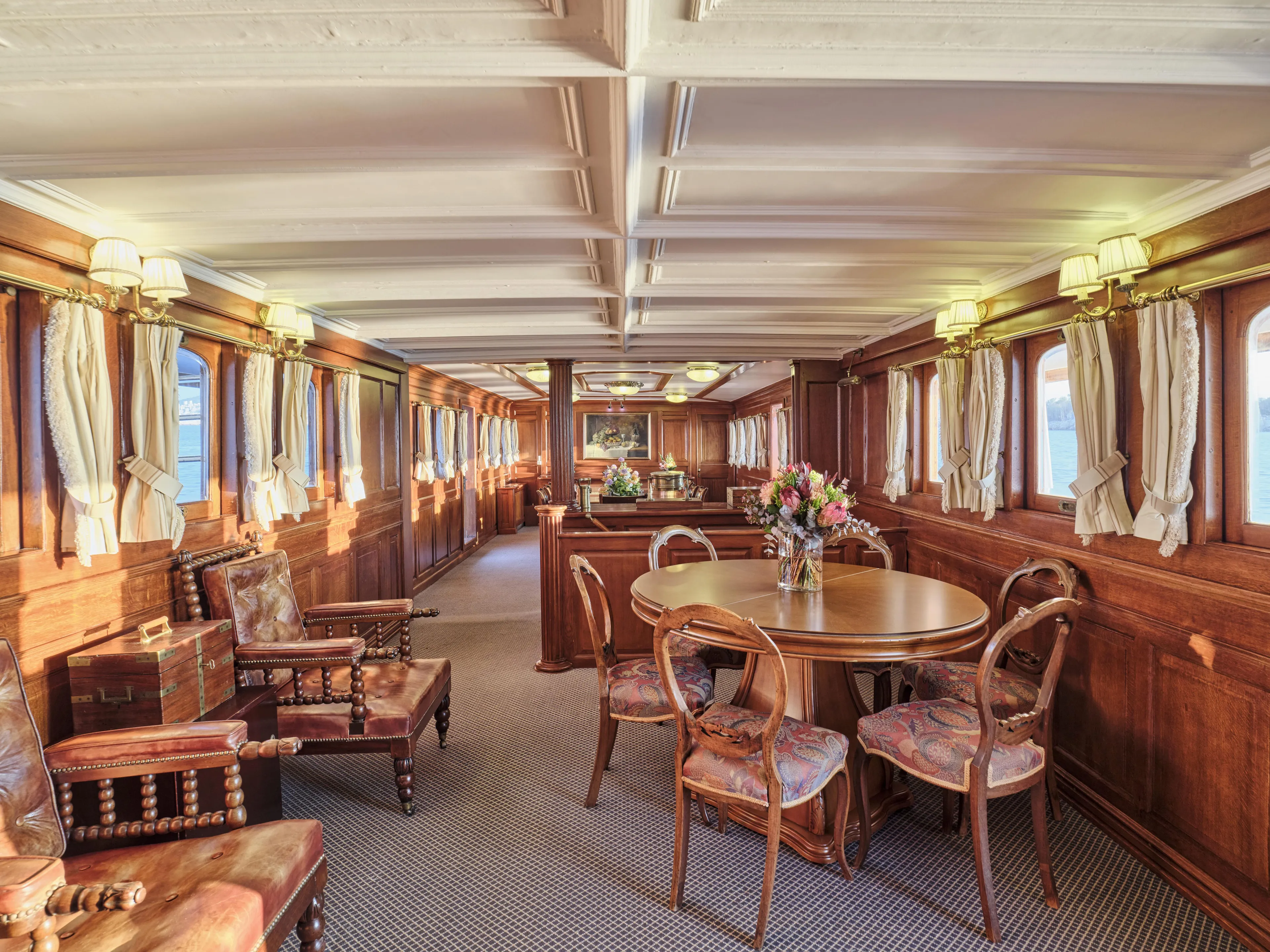 Luxurious vintage ship interior with wooden decor, elegant seating, and floral centerpiece, built in 1902.