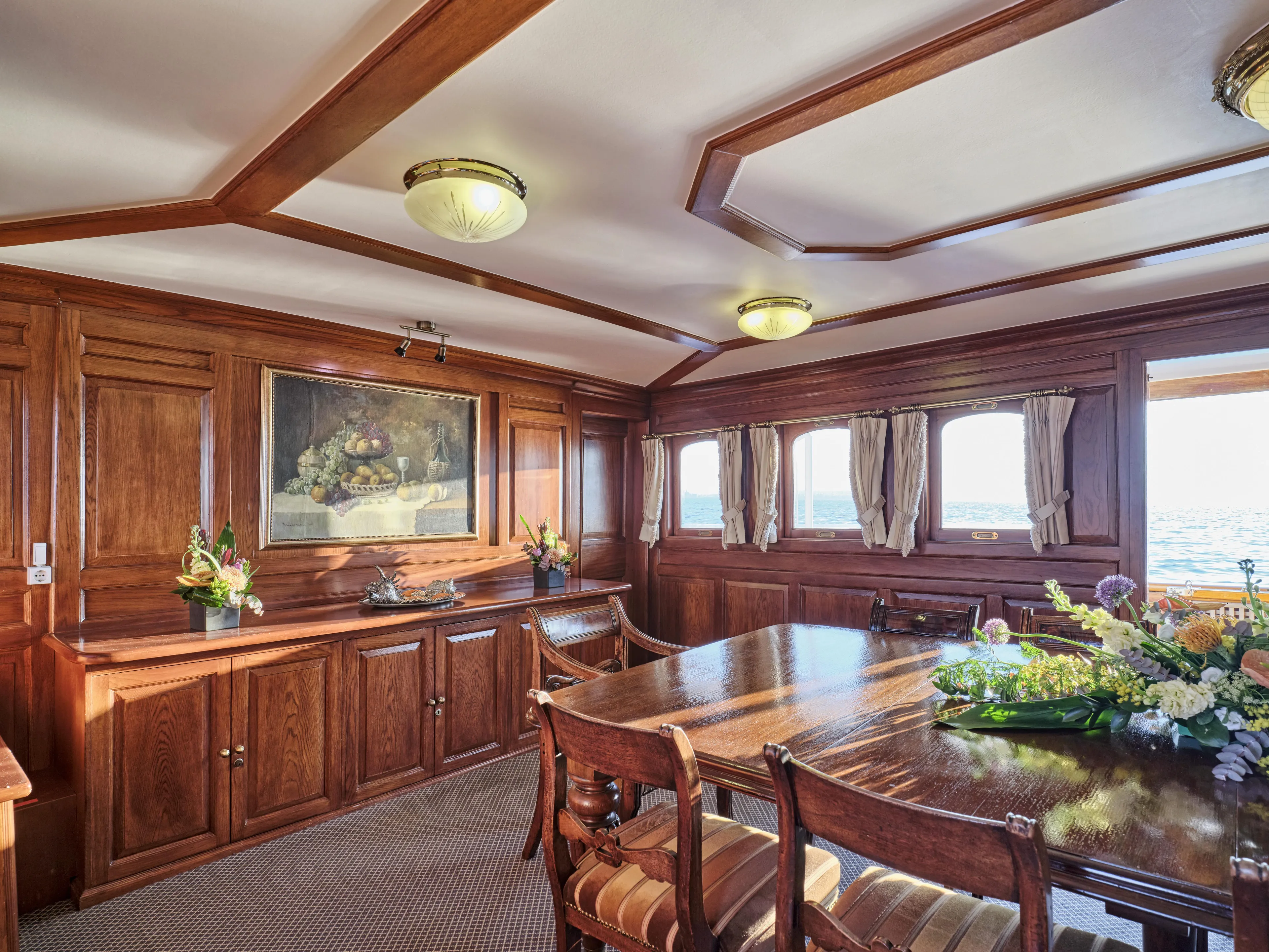 Luxurious wooden dining room on a 1902 Ailsa Shipbuilding vessel, featuring elegant decor and ocean views.