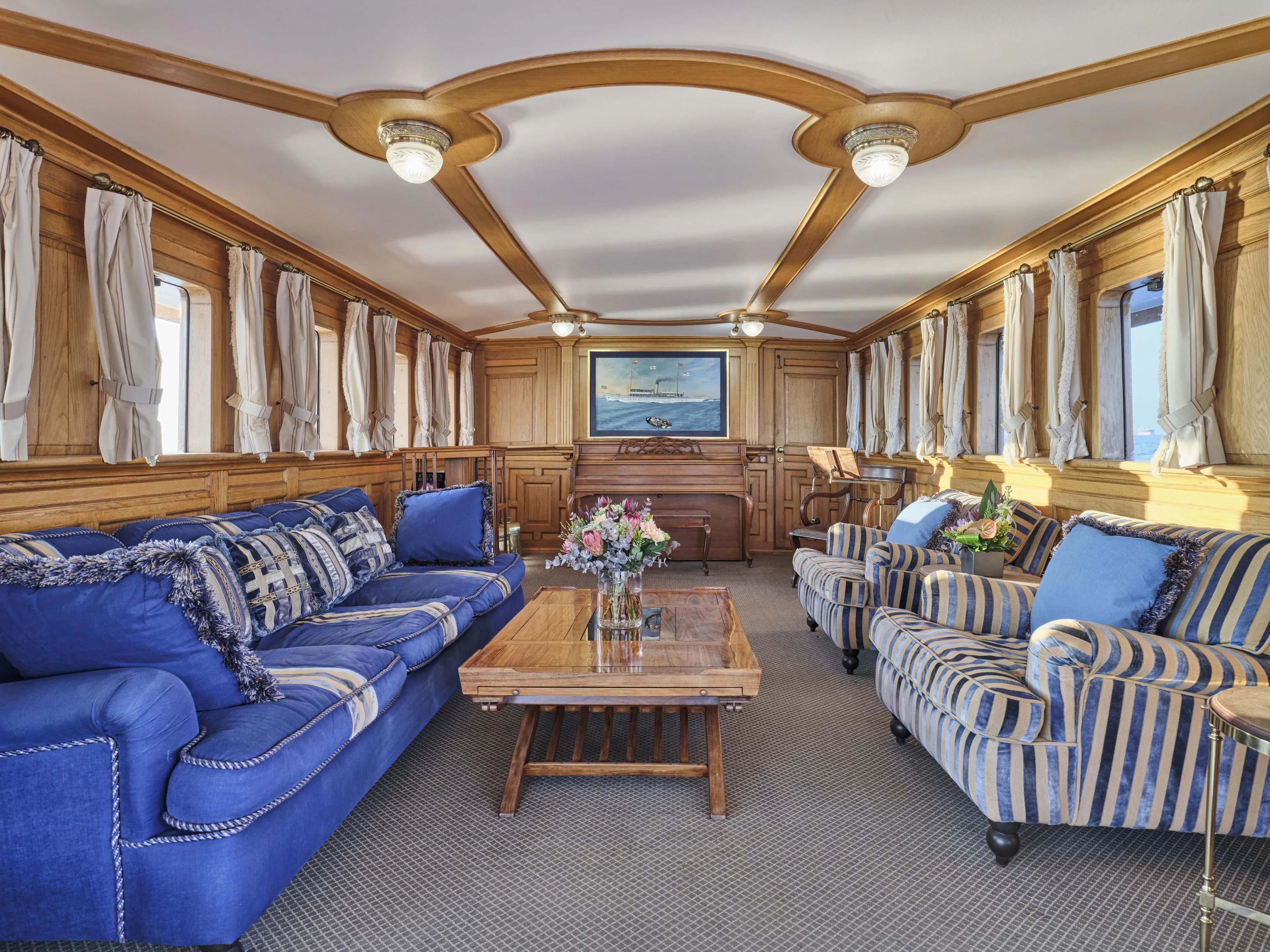 Luxurious ship interior with blue sofas, striped chairs, and elegant wood paneling, Ailsa Shipbuilding 1902.