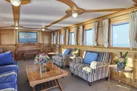 Luxurious ship interior with elegant wood paneling, striped armchairs, and floral arrangements, built in 1902.