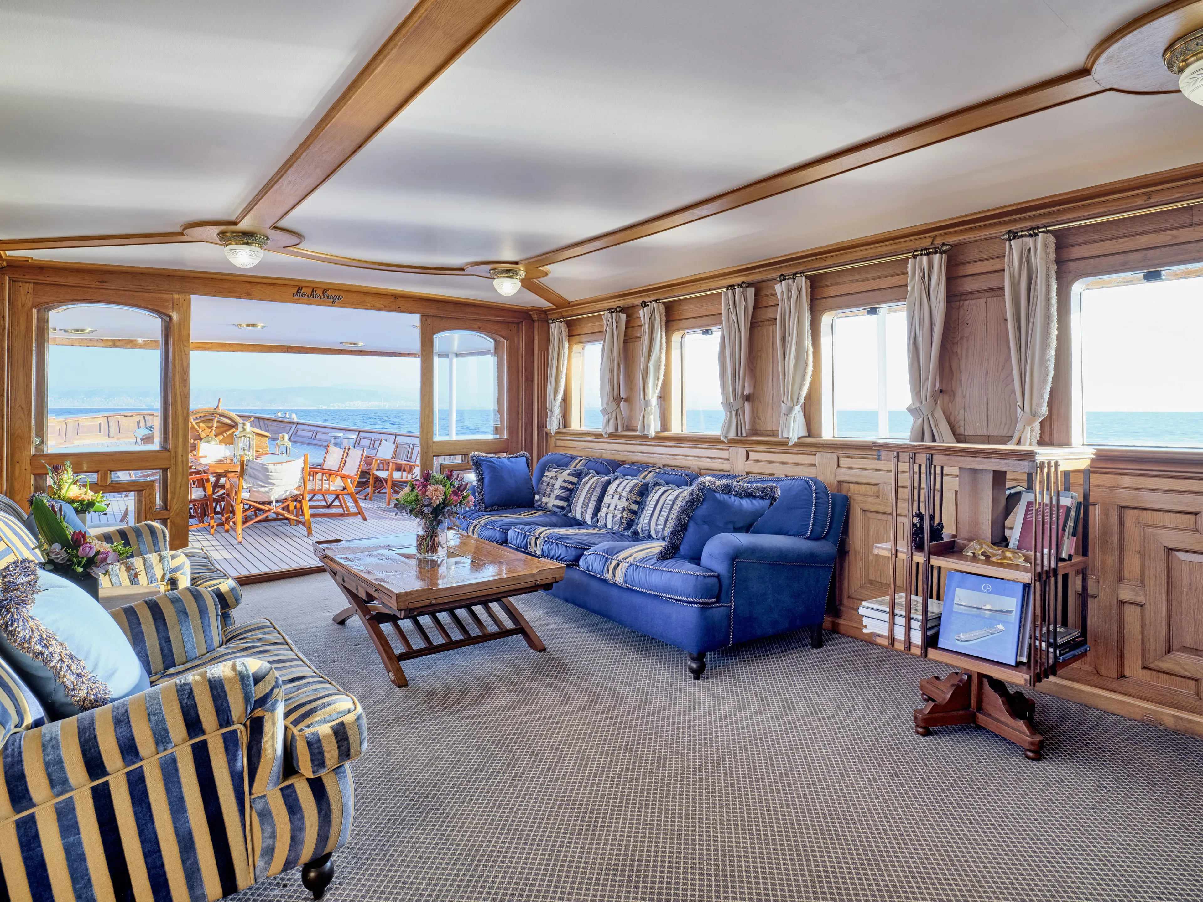 Luxurious ship interior with blue seating, wooden paneling, and ocean view, Custom Ailsa Shipbuilding, 1902.