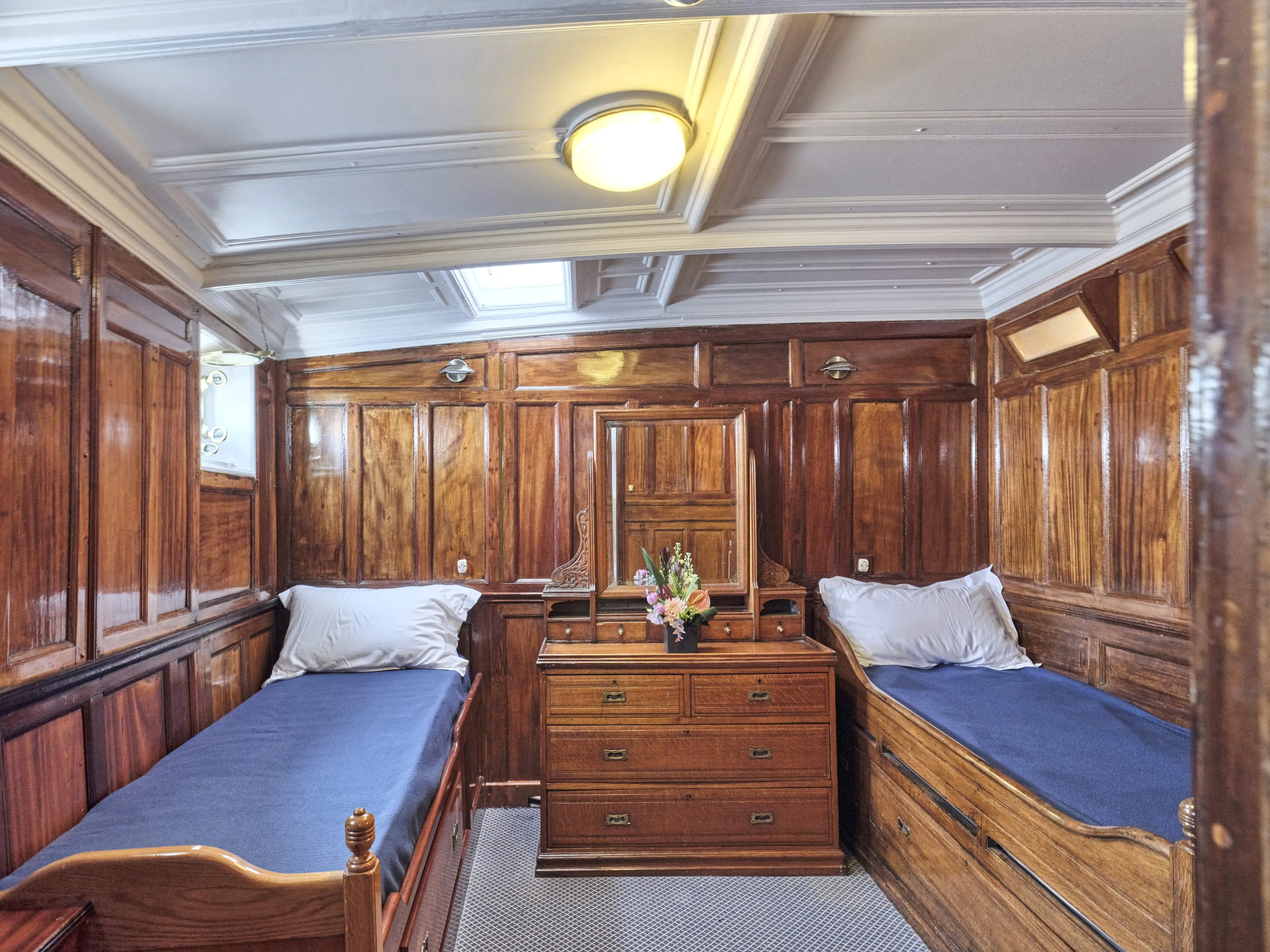Luxurious vintage ship cabin with wooden paneling, twin beds, and a central dresser, built in 1902.