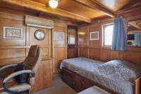 Cozy wooden ship cabin with bed, chair, and nautical decor, built by Ailsa Shipbuilding in 1902.