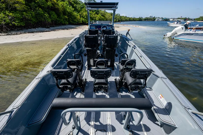  Yacht Photos Pics 2023 SAFE Boats Interceptor with seating, docked near a sandy shore and lush greenery.
