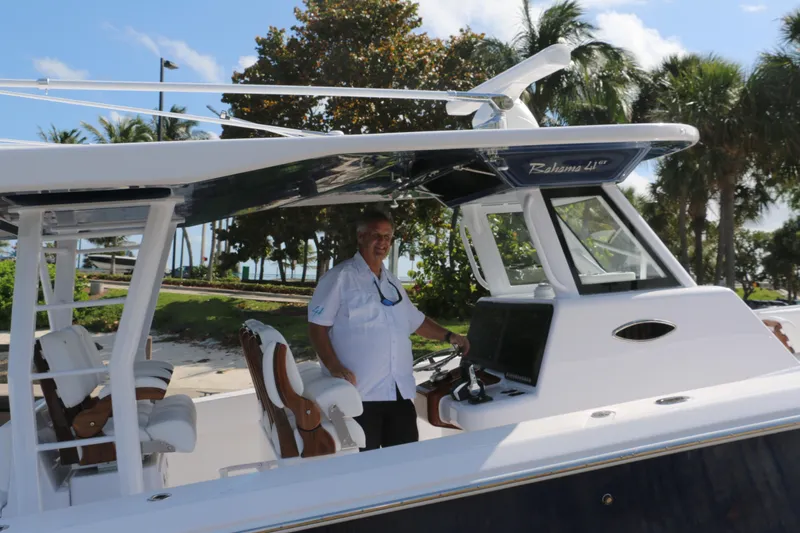  Yacht Photos Pics Man aboard 2026 Bahama 41 GT boat, docked with tropical background.