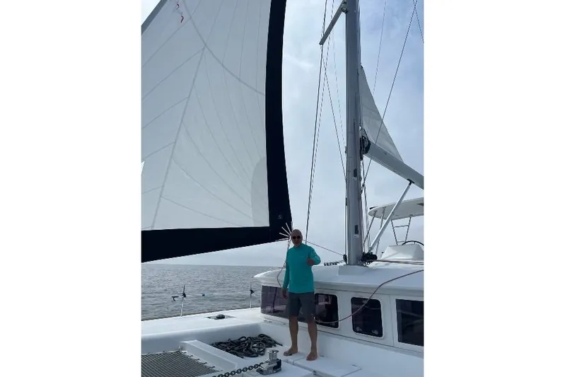 Whatif Yacht Photos Pics Man standing on a 2013 Lagoon 450 catamaran with sails raised on a calm sea.
